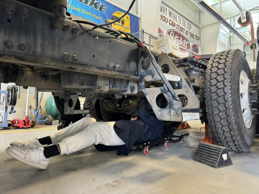 a student is working on the brakes under the truck